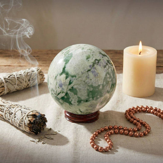 Peace Jade Sphere 66mm displayed in a spiritual setting with sage, candle, and beads, promoting emotional balance and harmony.