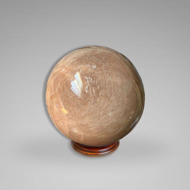 Polished Flashy Peach Moonstone Sphere — Nurturing & Balancing crystal on wooden base, showcasing its radiant peach-toned shimmer.