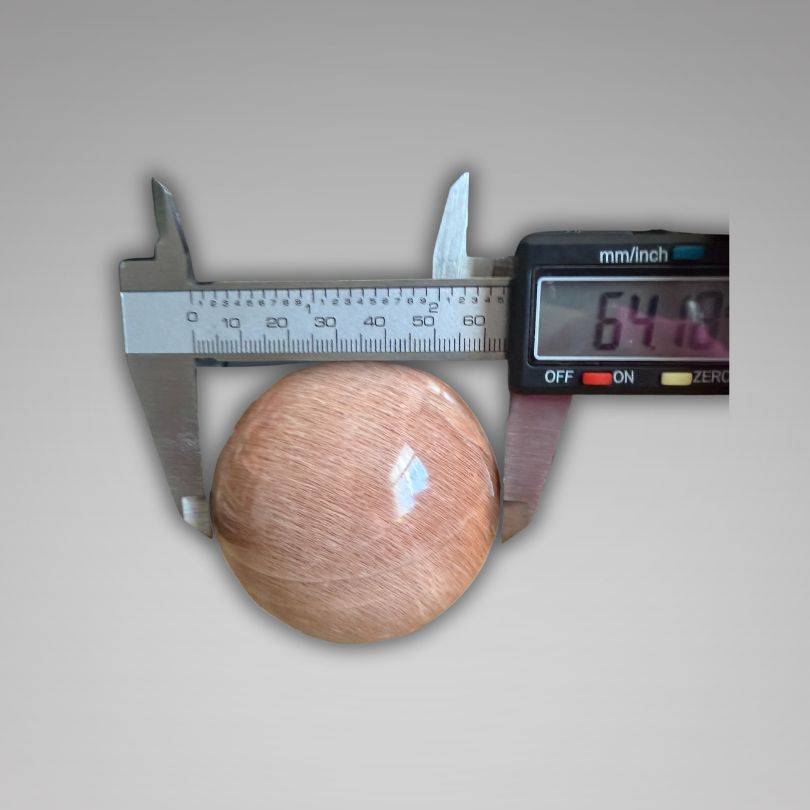 Flashy Peach Moonstone Sphere — Nurturing & Balancing measured at 64.10mm with digital caliper, highlighting gemstone size for collectors.