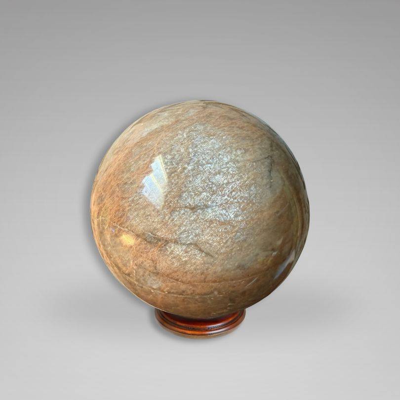 Large Flashy Peach Moonstone Sphere — Nurturing & Balancing crystal with natural inclusions and shimmer, displayed on a wooden stand.