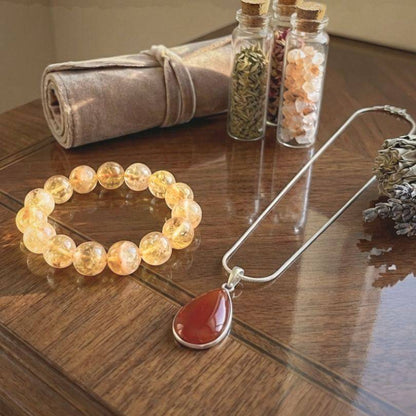 Path of Prosperity Aligned Pairing for Abundance curated bundle featuring a citrine bracelet and carnelian pendant necklace on a wooden table.