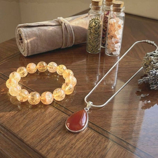 Path of Prosperity Aligned Pairing for Abundance curated bundle featuring a citrine bracelet and carnelian pendant necklace on a wooden table.