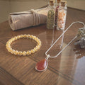 Path of Prosperity Aligned Pairing for Abundance curated bundle featuring a golden rutile quartz bracelet and carnelian pendant necklace on a wooden table.