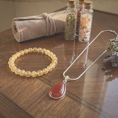 Path of Prosperity Aligned Pairing for Abundance curated bundle featuring a golden rutile quartz bracelet and carnelian pendant necklace on a wooden table.