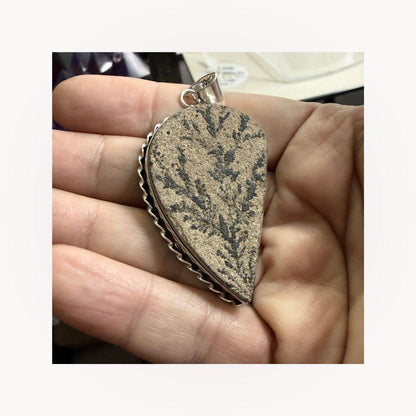 Hand holding Psilomelane Jasper Pendant with grounding lightning branch design. Natural stone set in silver teardrop frame.