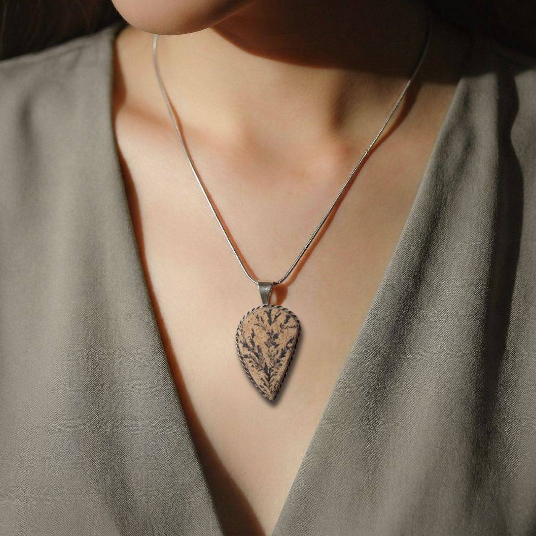Woman wearing Psilomelane Jasper Pendant with lightning branch design. Elegant teardrop shape enhances self-awareness and style.