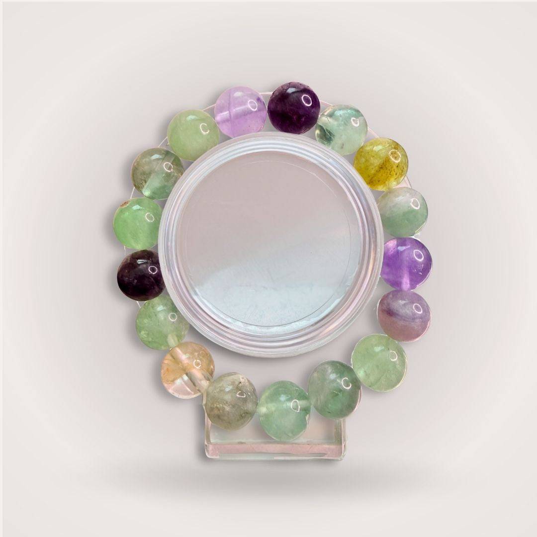 Rainbow Fluorite 12mm Beaded Bracelet for Clarity & Intuition featuring polished multicolor beads in green, purple, and yellow tones on display stand.