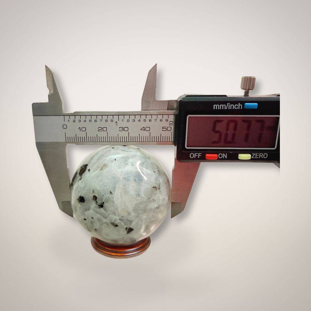 Digital caliper measuring 50.77mm Rainbow Moonstone Sphere, confirming size for collectors and spiritual practitioners.