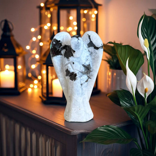 Decorative Rainbow Moonstone angel statue on a wooden surface with candles and fairy lights in the background