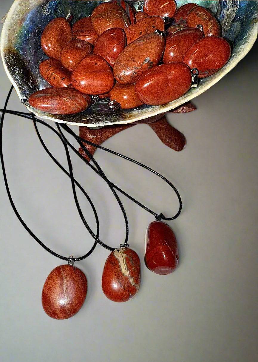 Shell bowl filled with polished red jasper tumble pendants in warm earthy tones, each set with silver bales on 20' waxed cotton cords.