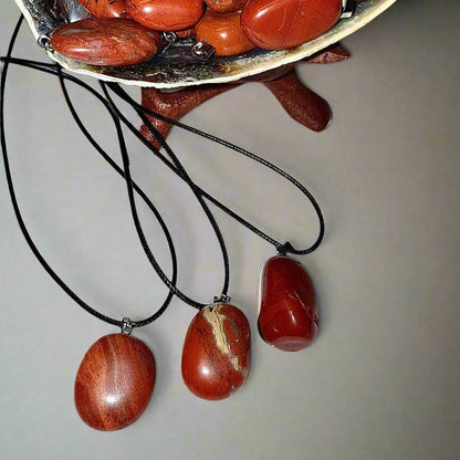 Shell bowl filled with polished red jasper tumble pendants in warm earthy tones, each set with silver bales on 20' waxed cotton cords.