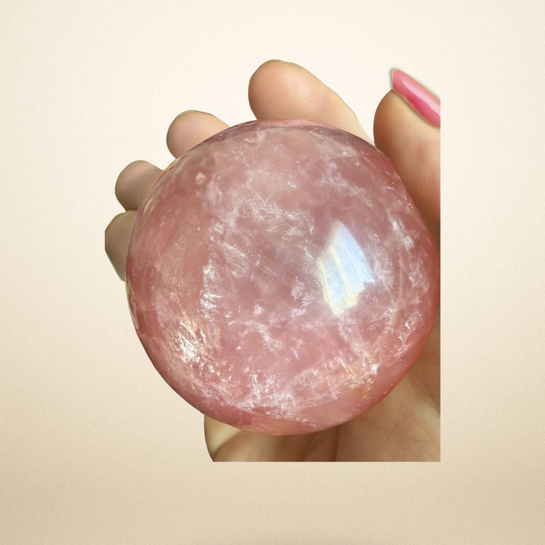 Hand holding a polished Rose Quartz Sphere 350–400g from Madagascar, highlighting its translucent pink color and emotional healing properties.