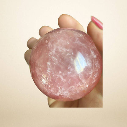 Hand holding a polished Rose Quartz Sphere 350–400g from Madagascar, highlighting its translucent pink color and emotional healing properties.