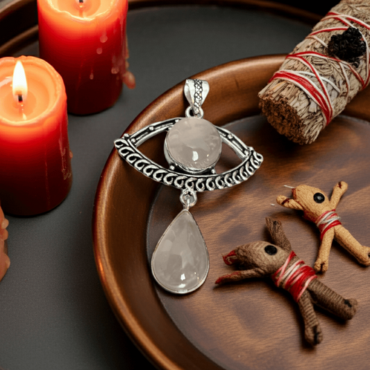 Rose Quart Evil Eye Drop Pendant on a wooden plate with candles and other items
