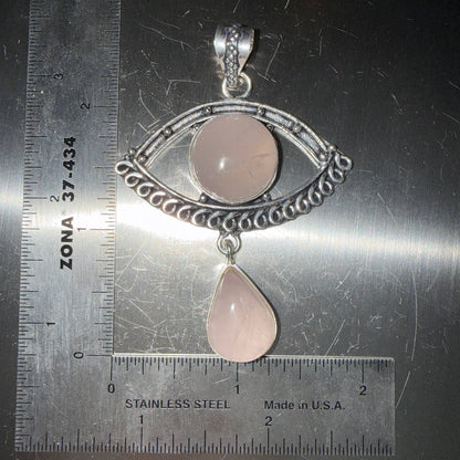 Rose Quartz Evil Eye pendant with a rose quartz drop in a silver setting on a metallic surface with ruler for scale.