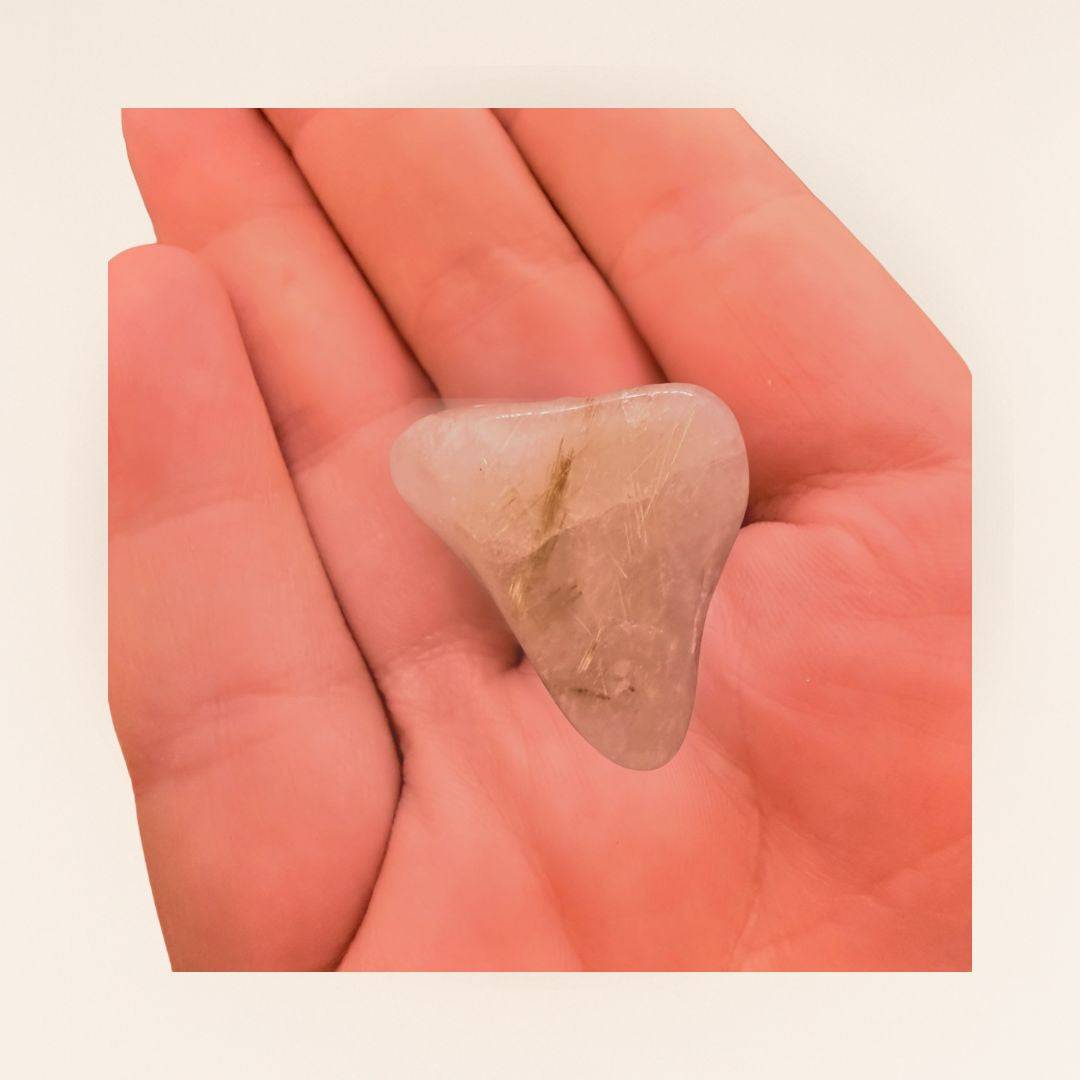 Hand holding a Rutilated Quartz Tumbled Stone (Gold Rutile), showcasing its clarity and golden rutile strands for psychic connection use.
