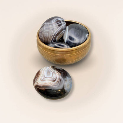 Collection of medium Sardonyx palm stones in a brass bowl, showcasing polished finishes and natural earthy patterns for crystal healing.