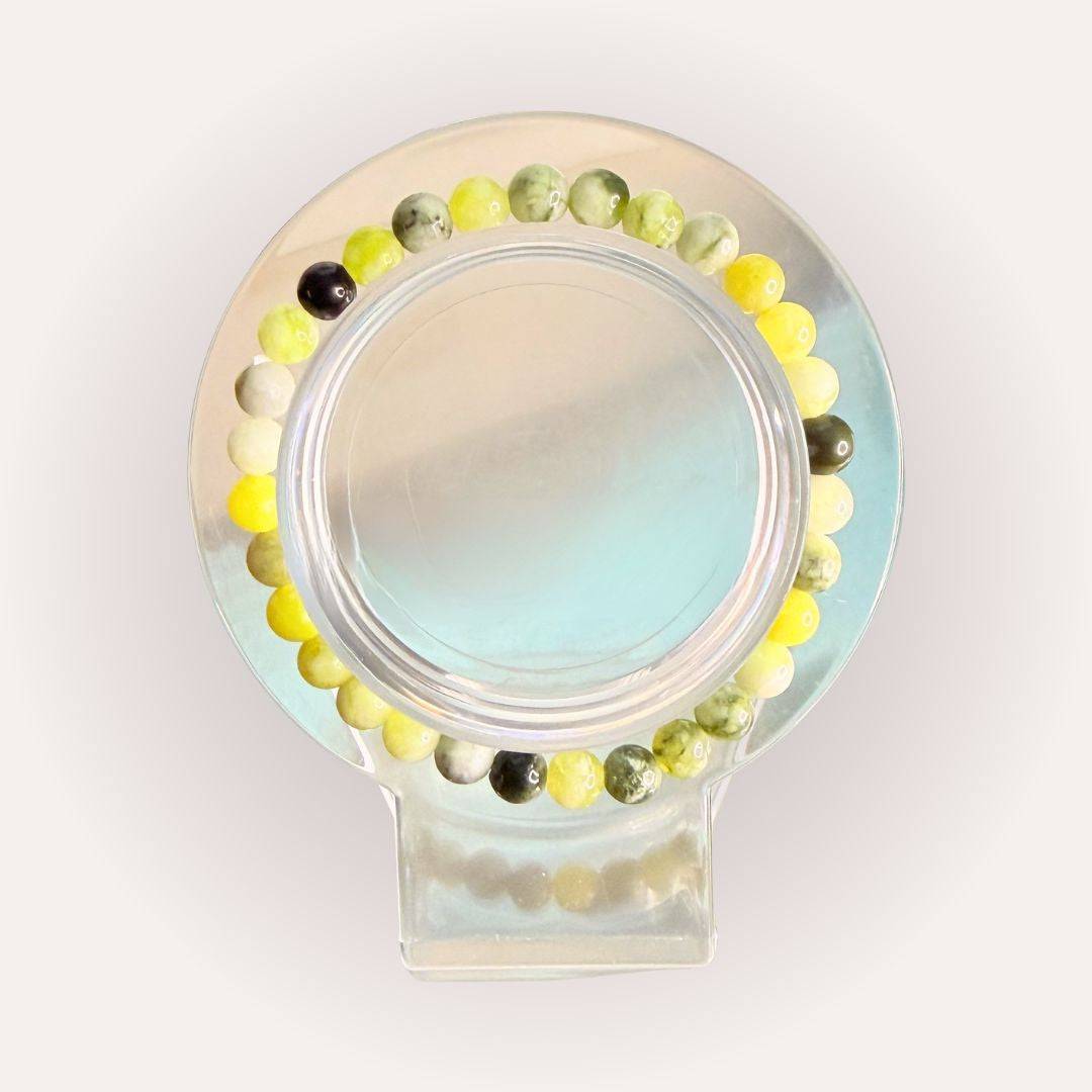 Serpentine Bracelet 6mm from South Africa with green and yellow beads, displayed on a clear circular stand. Ideal for cleansing and renewal.