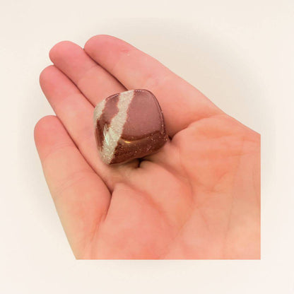 Hand holding a Shiva Lingam Cube tumbled stone, showcasing its compact size and unique maroon-beige pattern for spiritual vitality.