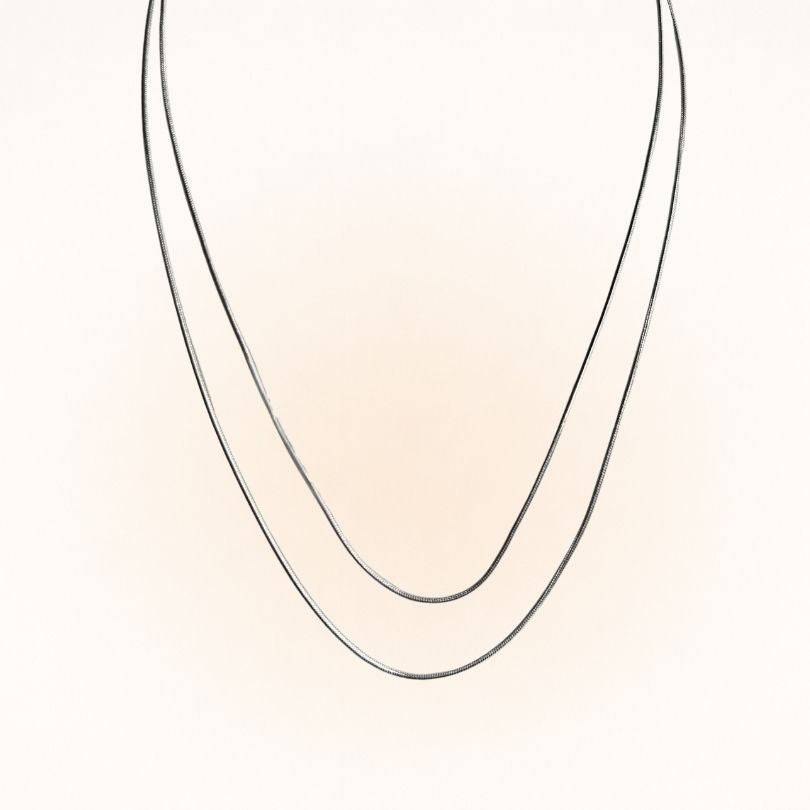 Two Silver Snake Chain Necklaces in different lengths shown in a draped V-shape. Perfect for layering with other jewelry pieces.