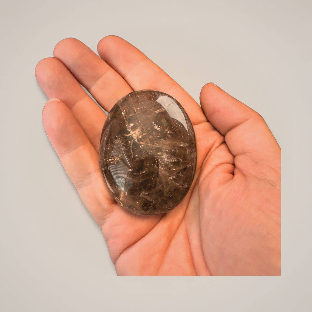 Smoky Quartz palm stone held in hand with crystals and decorative items