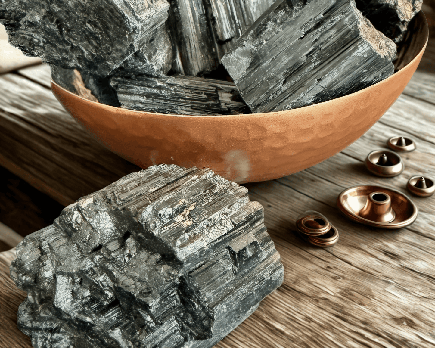 Close-up of chunky Brazilian black tourmaline crystals in a hammered copper bowl with one specimen in the foreground showing vertical striations.