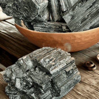 Close-up of chunky Brazilian black tourmaline crystals in a hammered copper bowl with one specimen in the foreground showing vertical striations.
