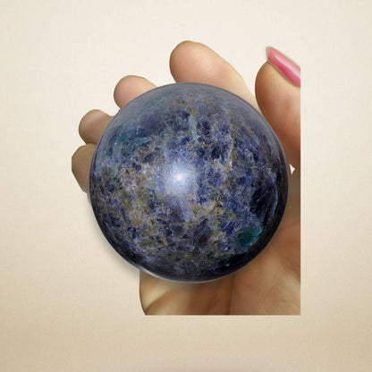 Hand holding the Trinity Stone Sphere 348g, highlighting its polished surface and vibrant mix of Fuchsite, Kyanite, and Garnet minerals.