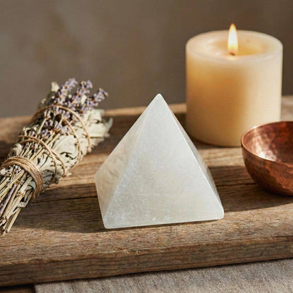 White Selenite Pyramid | Calm Awareness, Energy Cleansing placed on a wooden table with sage, candle, and copper bowl for meditation décor.