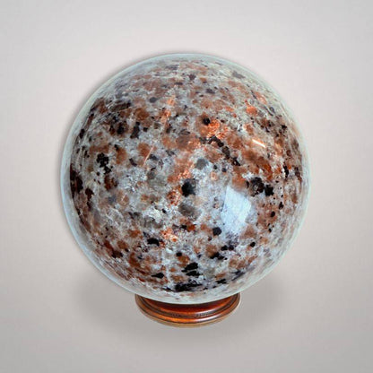 UV Sodalite 'Yooperlite' Sphere 464g with polished surface, showcasing natural orange and black mineral patterns on a display stand.