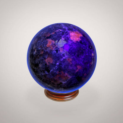UV Sodalite (Yooperlite) Sphere 58mm strong glowing under UV light with vibrant purple and orange fluorescence, highlighting its rare mineral quality.