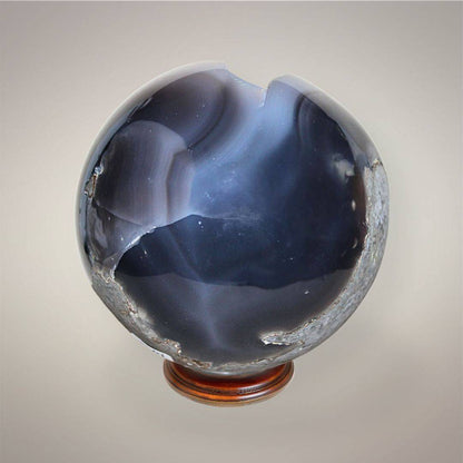 Back view of Brazilian Agate druzy sphere showing smoky gray-blue chalcedony banding, polished surface, exposed matrix, and natural openings.