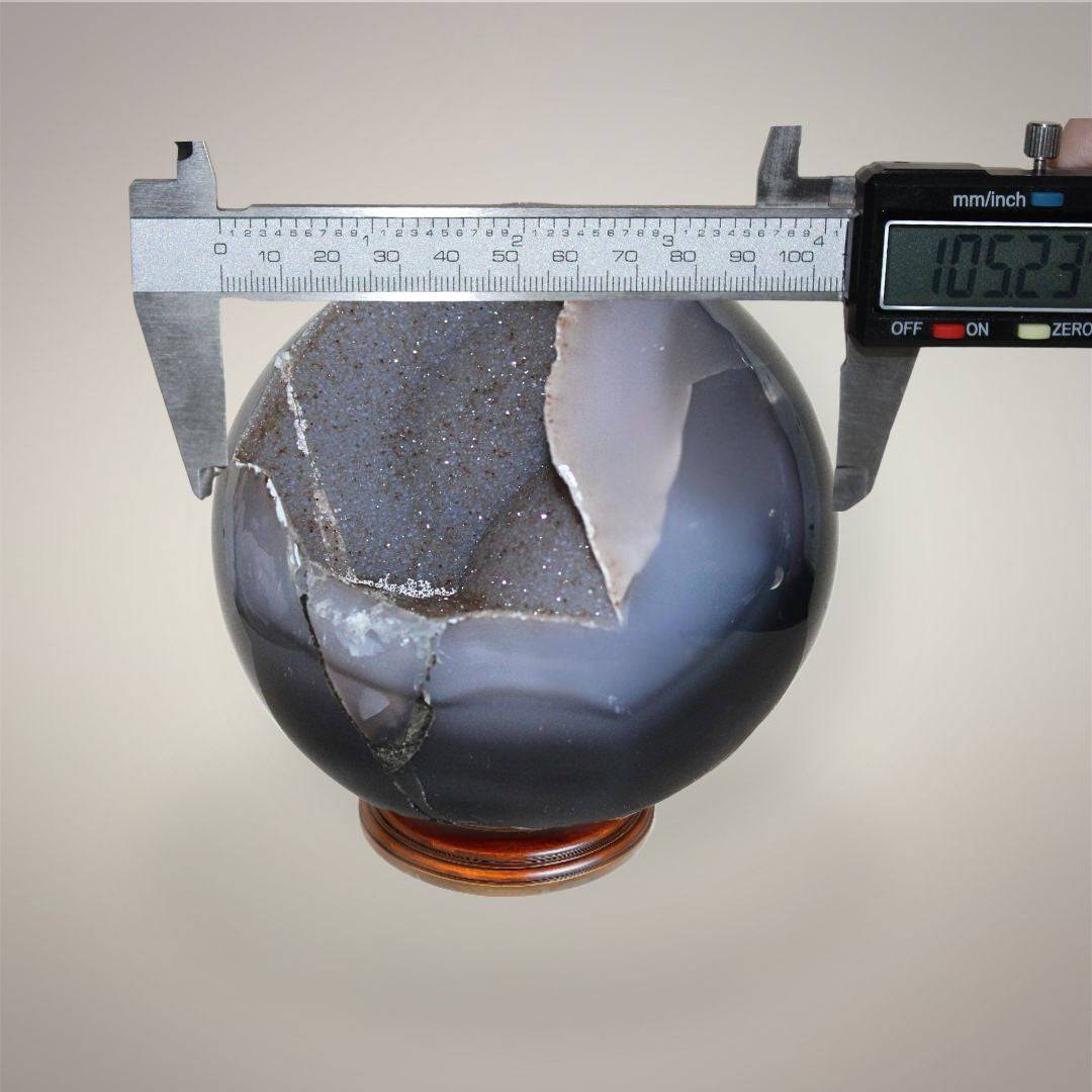 Large Brazilian Agate druzy sphere measured with digital calipers at approximately 105.23 mm diameter.