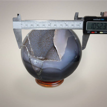 Large Brazilian Agate druzy sphere measured with digital calipers at approximately 105.23 mm diameter.