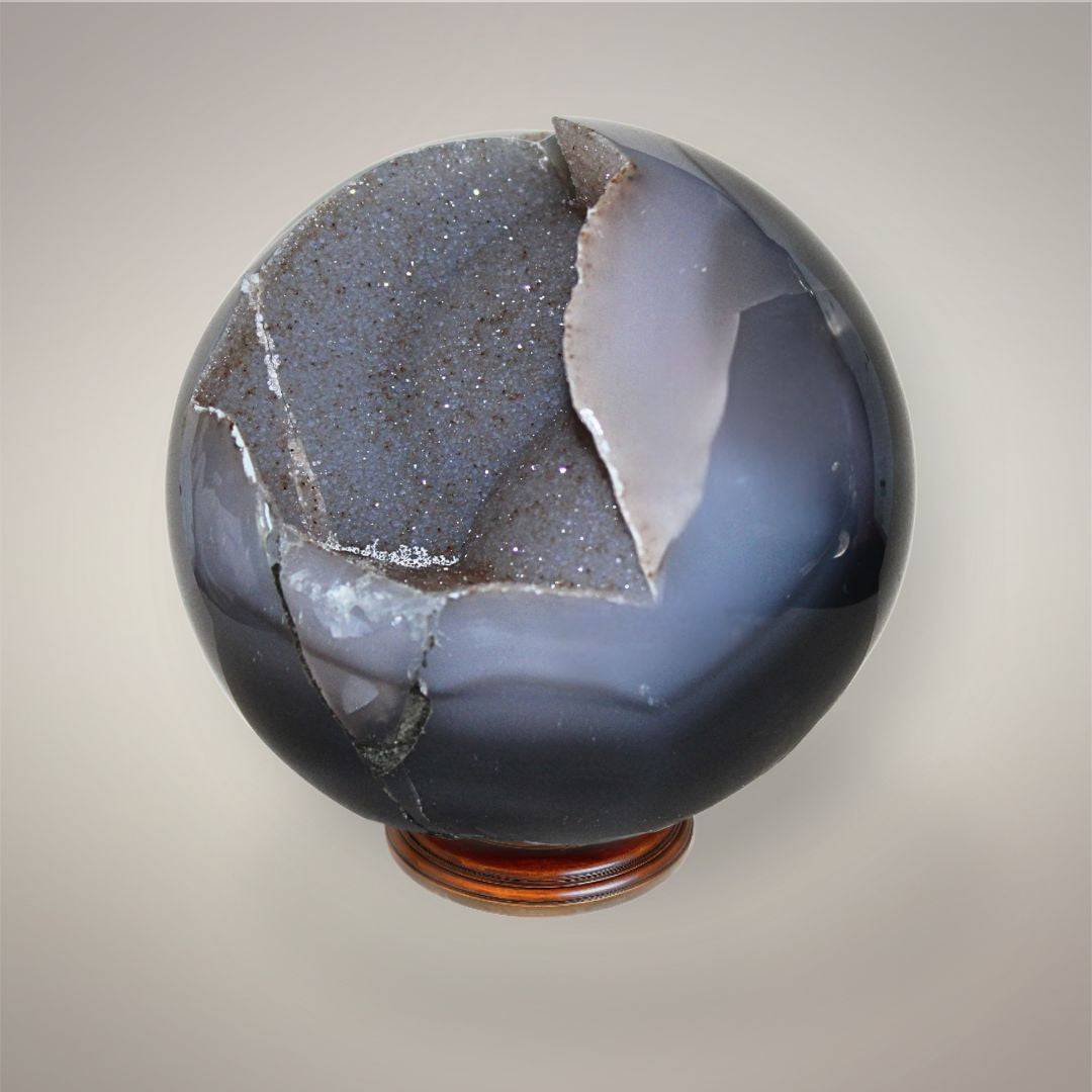 Side view of Agate druzy sphere showing polished dark chalcedony, exposed gray matrix, and the edge of the sparkling druzy pocket.
