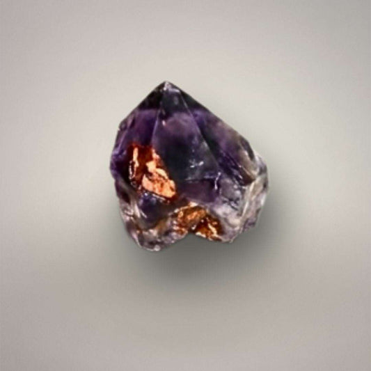 Close-up of a natural Alien Amethyst point with deep purple quartz and coppery hematite inclusions