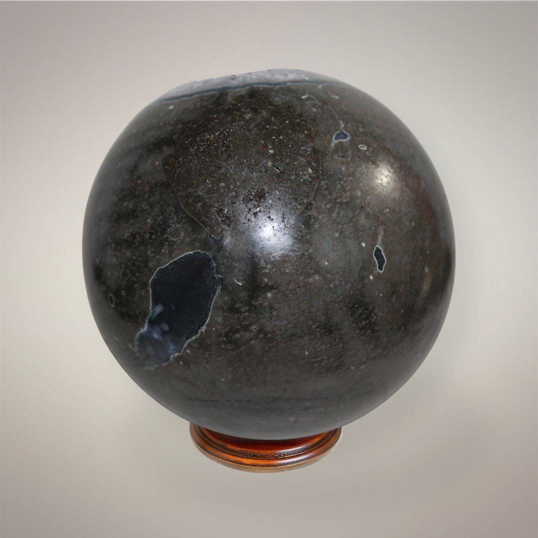 Back view of large Brazilian Amethyst geode sphere showing dark polished exterior with natural surface openings, matrix, and polish-related fractures.