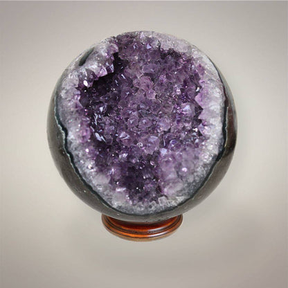Large Amethyst geode sphere from Brazil with deep violet crystal points, polished dark outer shell, and open sparkling geode pocket.