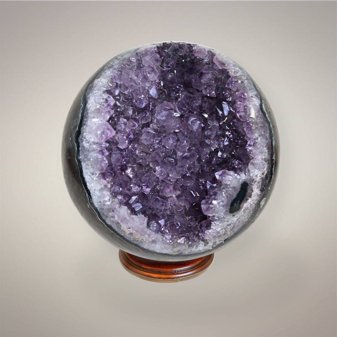 Amethyst geode sphere showing lavender and deep purple crystal points framed by white quartz and dark polished outer matrix.