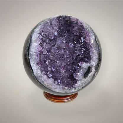 Amethyst geode sphere showing lavender and deep purple crystal points framed by white quartz and dark polished outer matrix.