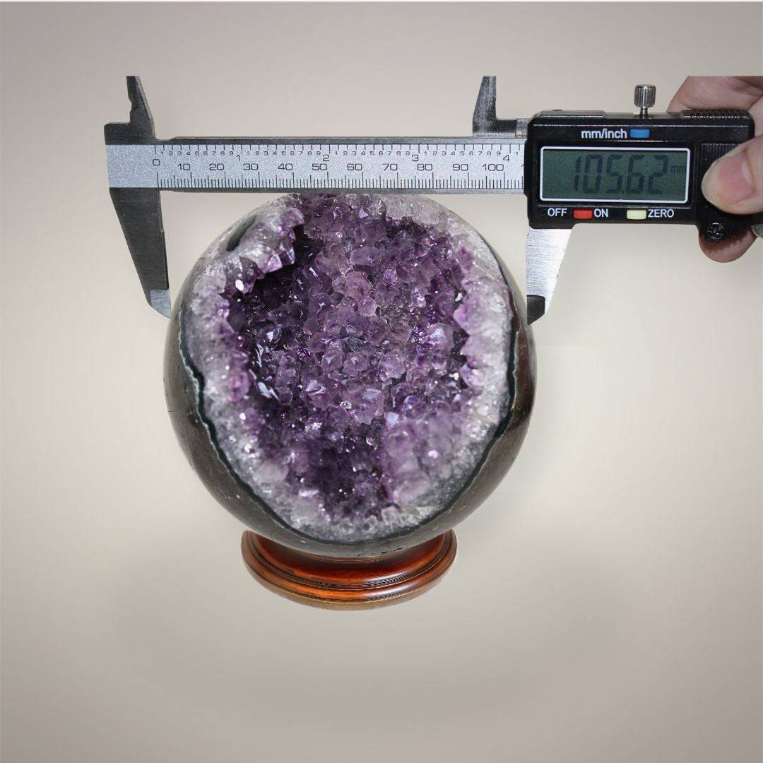 Large Brazilian Amethyst geode sphere measured with digital calipers at approximately 105.62 mm diameter.