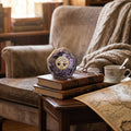 Amethyst orgonite dodecahedron displayed on vintage books with glasses, tea cup, map, and cozy reading chair