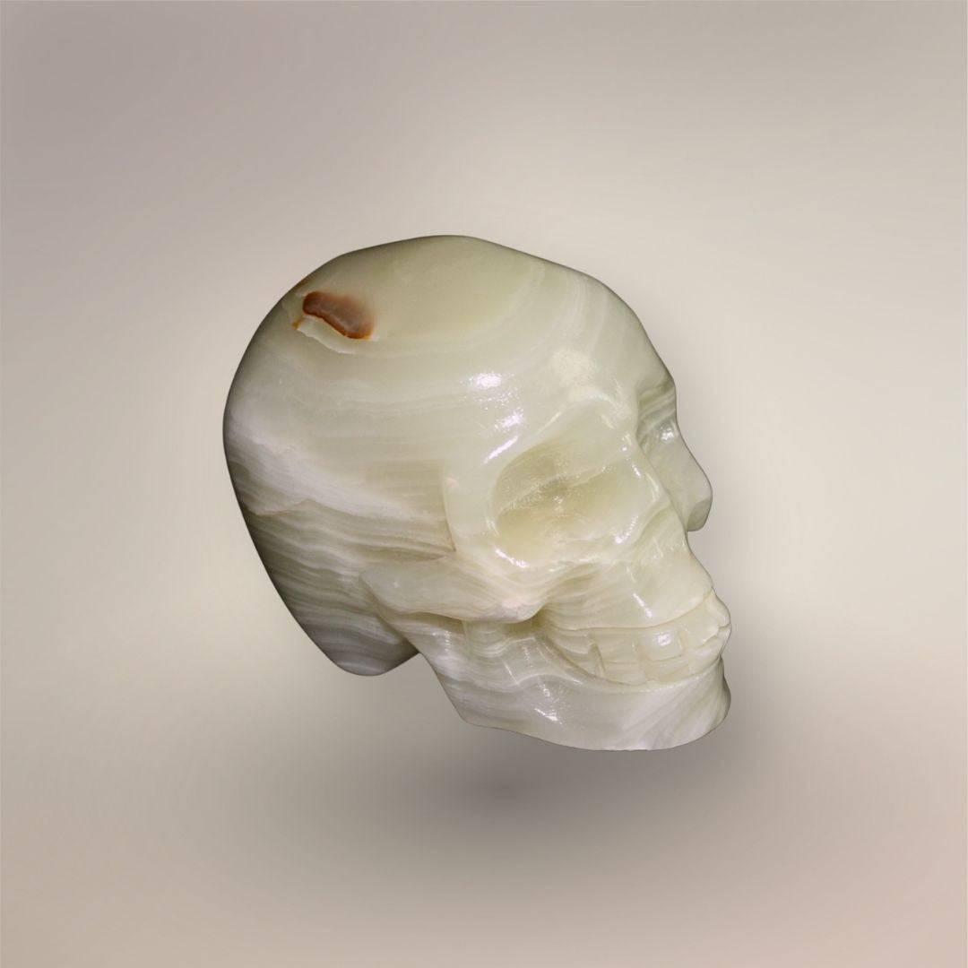 Hand-carved banded calcite skull from Mexico with cream-white layered banding, polished surface, and natural brown mineral marking.