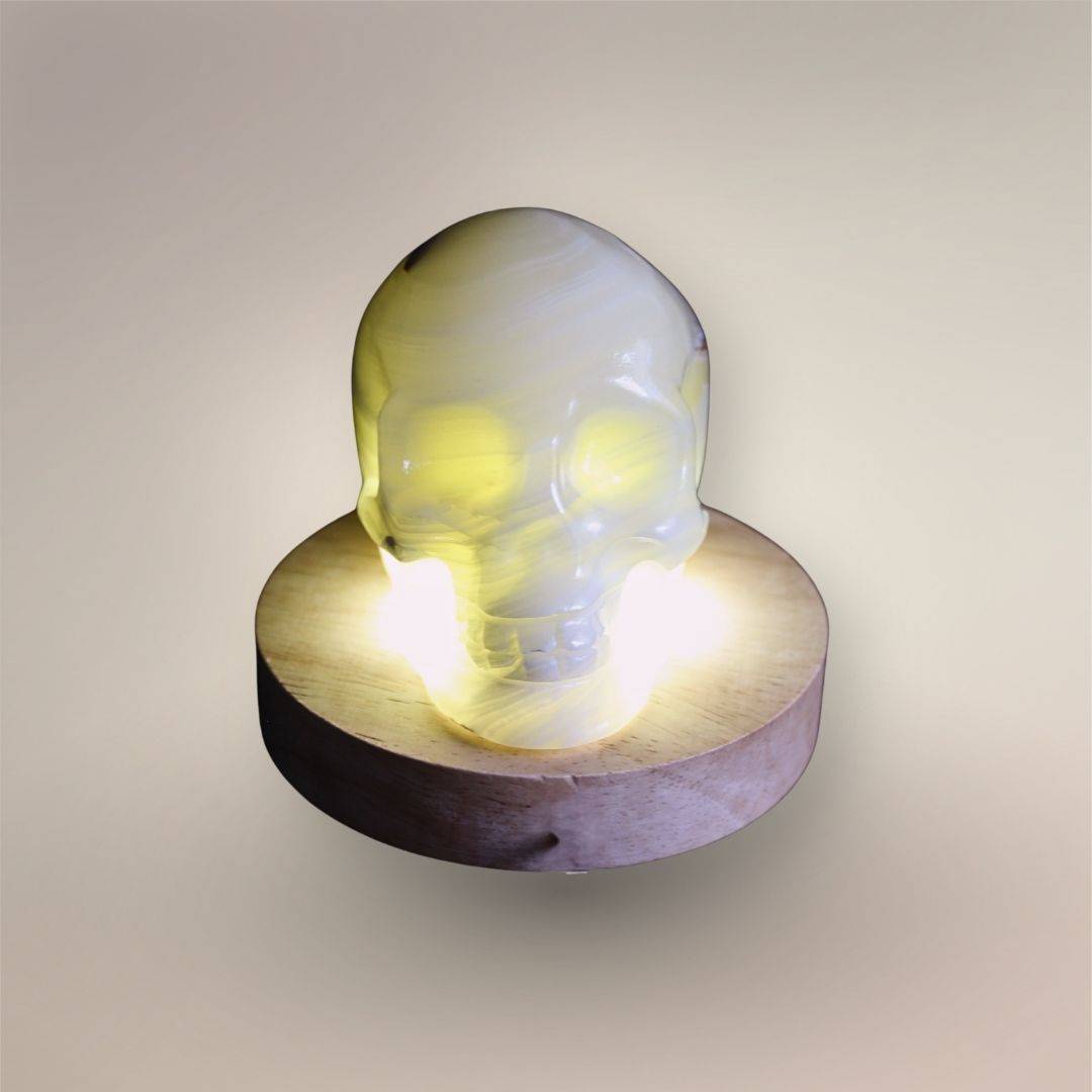 Front view of Mexican banded calcite skull illuminated from below, revealing translucent layered structure through the carving.