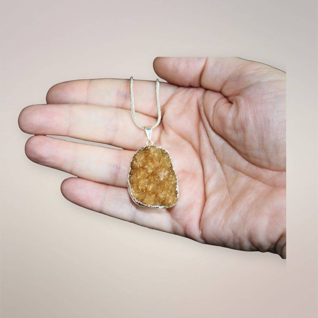 Citrine drusy pendant held in hand showing approximate 40 by 30 mm size and golden crystal face 