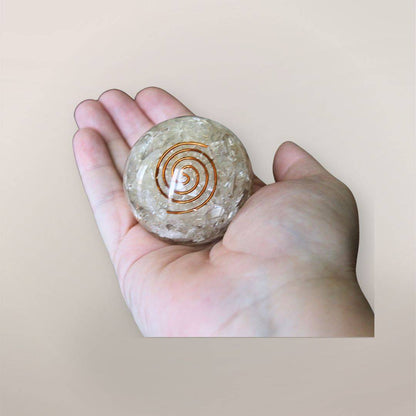 Two inch clear quartz orgonite sphere with copper spiral resting in a hand to show size and scale