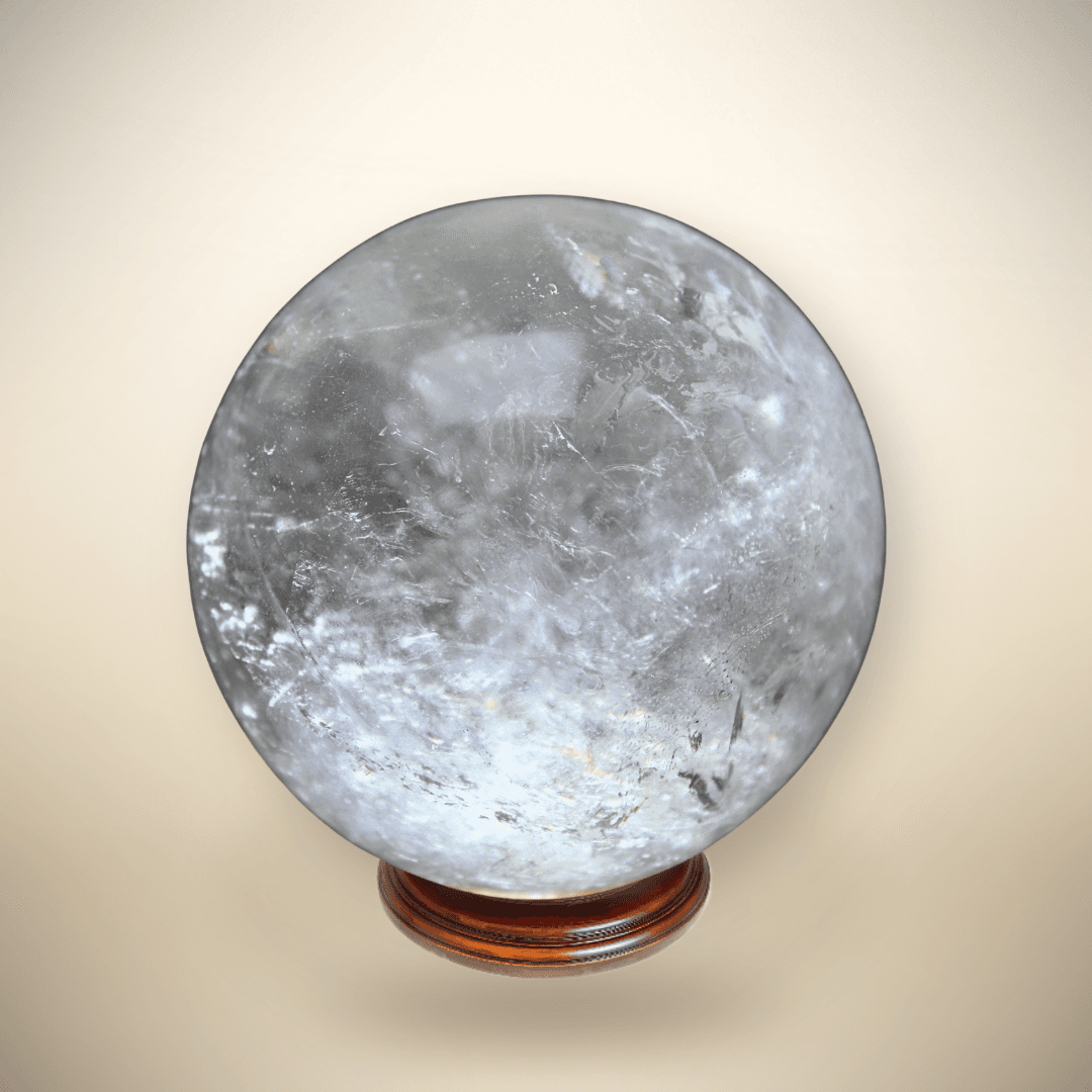 olished Clear Quartz sphere from Madagascar showing transparent quartz, white internal veils, and reflective formations on a wooden display stand.