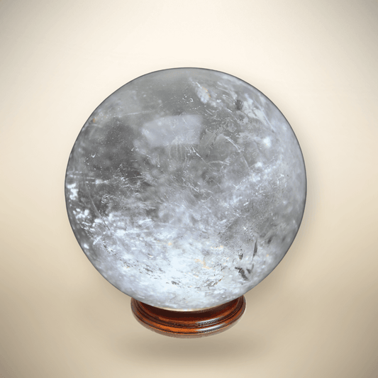 olished Clear Quartz sphere from Madagascar showing transparent quartz, white internal veils, and reflective formations on a wooden display stand.