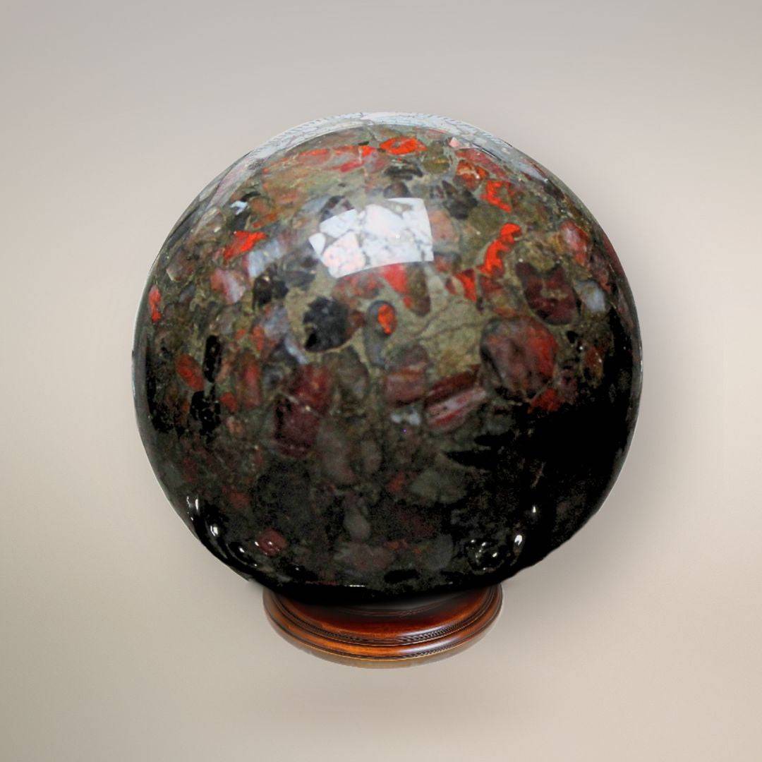 Reverse view of a polished Conglomerate Jasper sphere on a wooden stand, revealing different patterns of red jasper and quartz suspended in the dark stone.