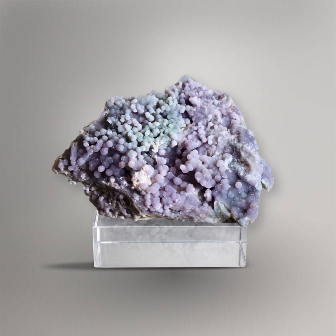 Front view of 335g Grape Agate cluster with dense lavender spheres and a pale blue-green center displayed on a clear block